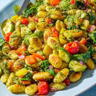 A close up photo of crispy gnocchi with pesto on a serving platter with a spoon.