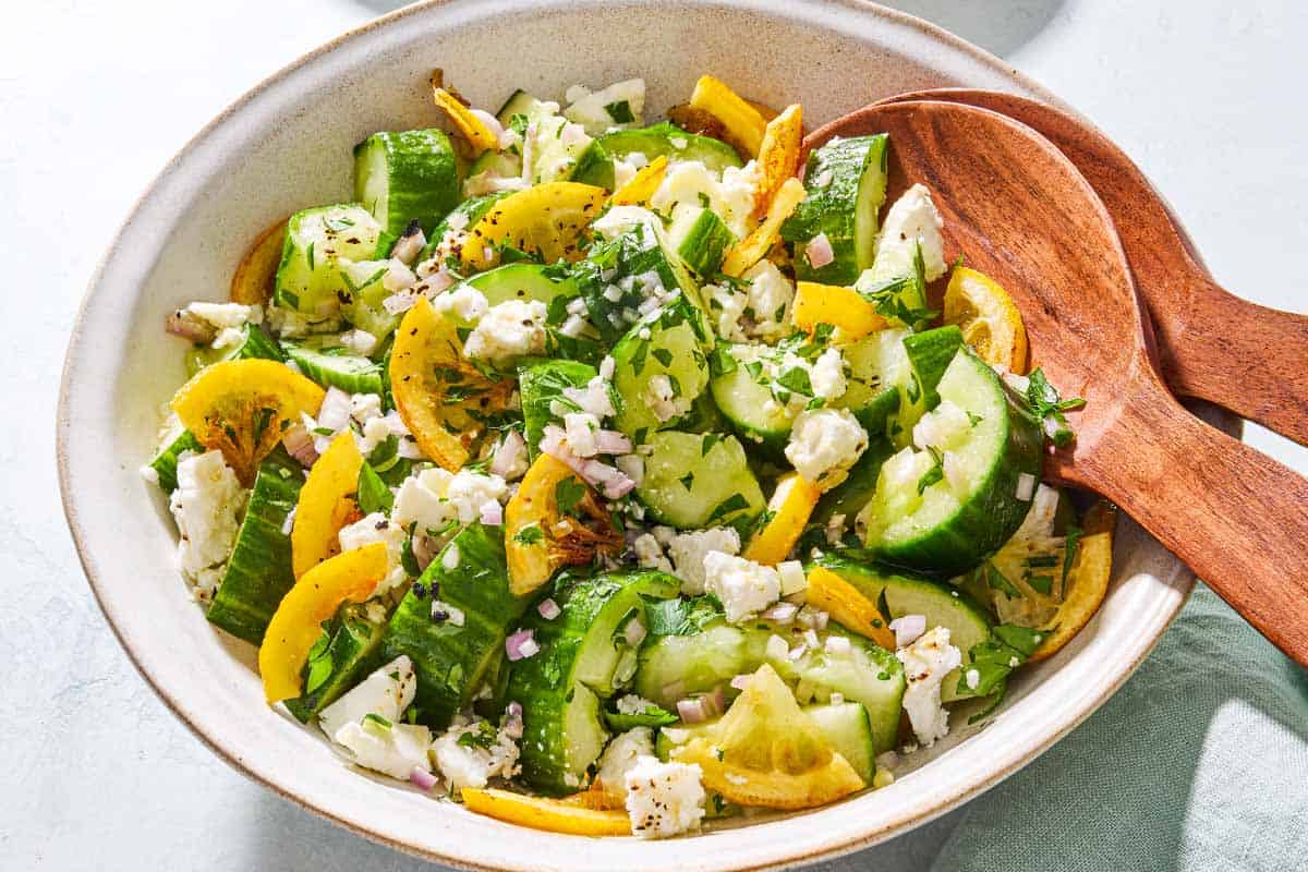 Smashed cucumber salad in a serving bowl with wooden serving utensils.