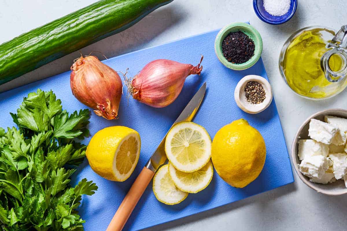 Ingredients for smashed cucumber salad including lemons, olive oil, salt, English cucumber, shallots, parsley, feta, urfa biber and black pepper.