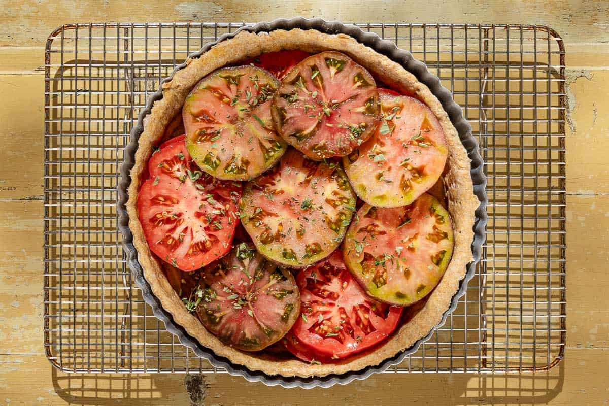 An overhead photo of an unbaked tomato tart in a tart pan sitting on a wire rack.