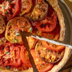 An overhead photo of a tomato tart on a plate on a wooden cutting board with one slice cut from it.