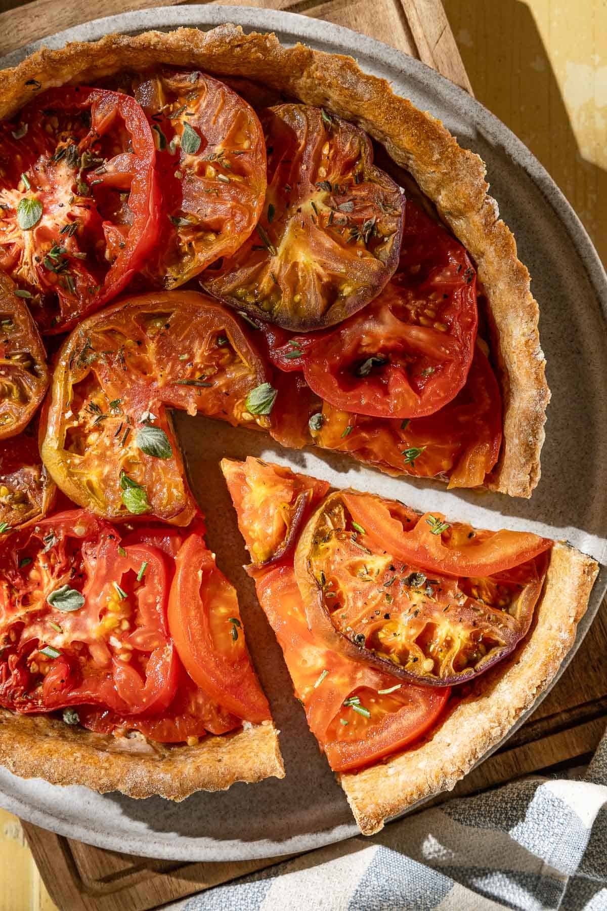 An overhead photo of a tomato tart on a plate on a wooden cutting board with one slice cut from it.