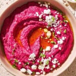 An overhead close up photo of beet hummus in a bowl topped with olive oil, feta cheese and parsley.