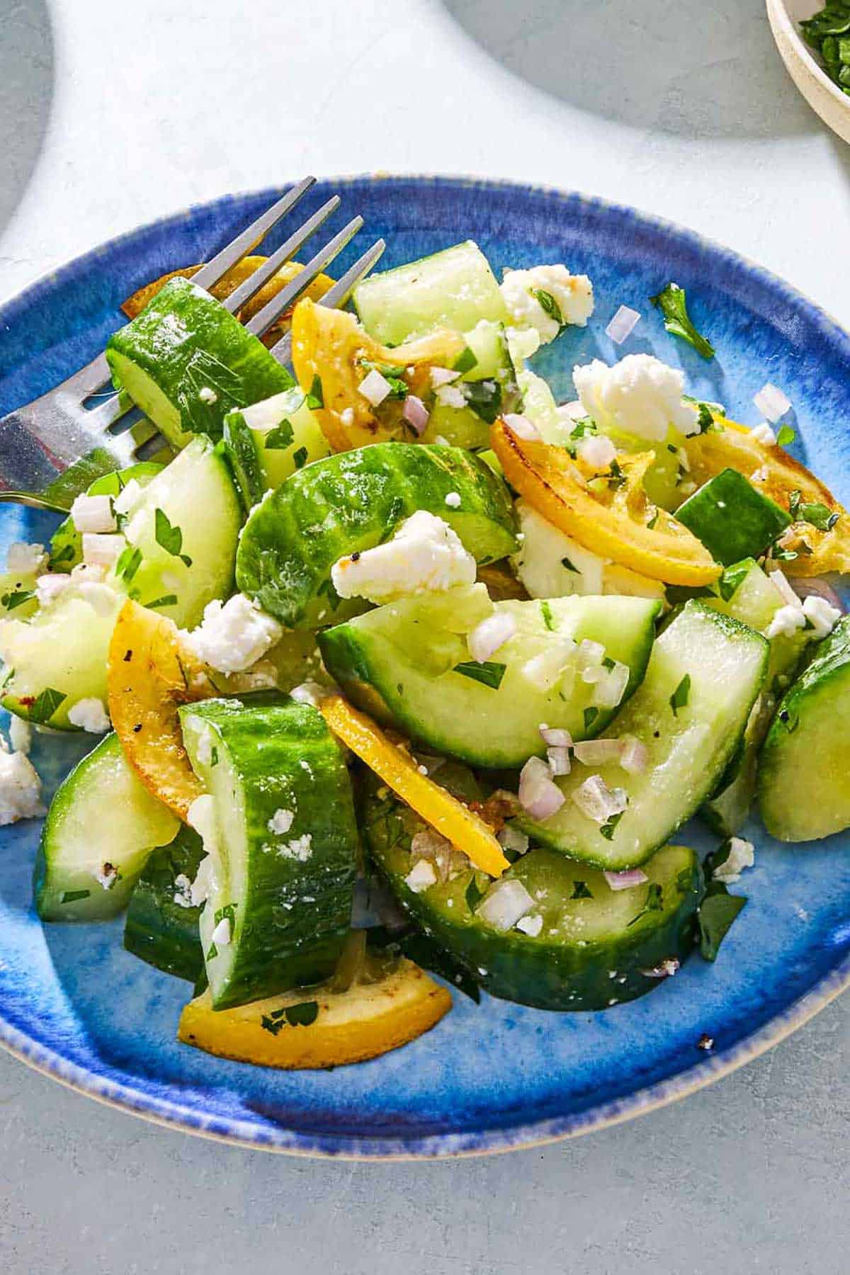 A close up of a smashed cucumber salad on a plate with a fork.