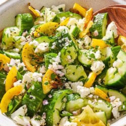 Smashed cucumber salad in a serving bowl with wooden serving utensils.