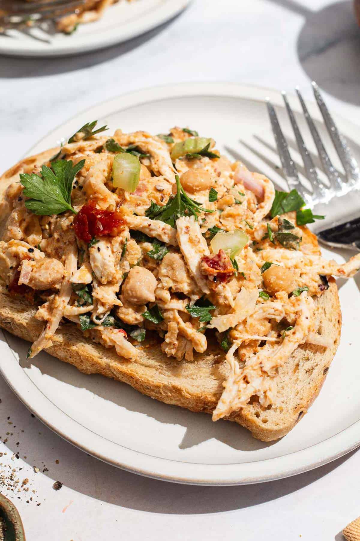 A close up of chickpea chicken salad on a slice of bread on a plate with a fork.