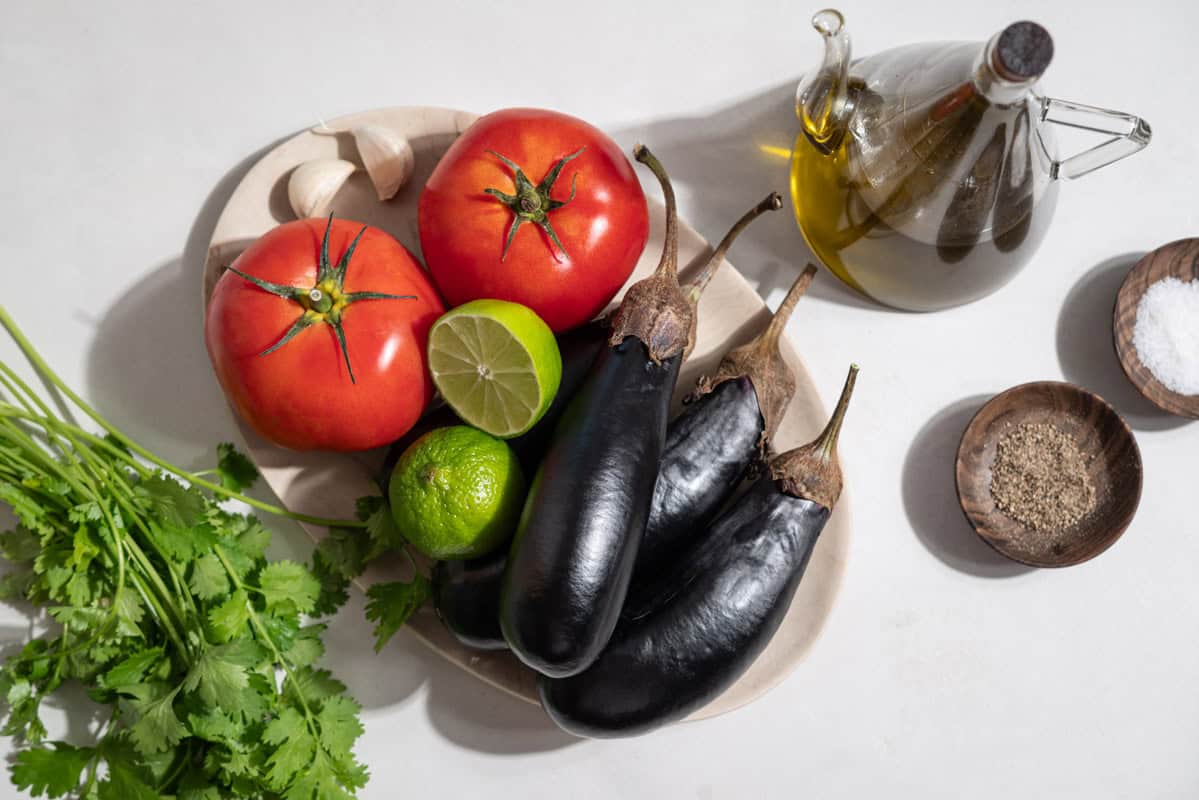 The ingredients for eggplant bruschetta including small globe eggplants, salt, black pepper, olive oil, tomatoes, lime, garlic and cilantro.