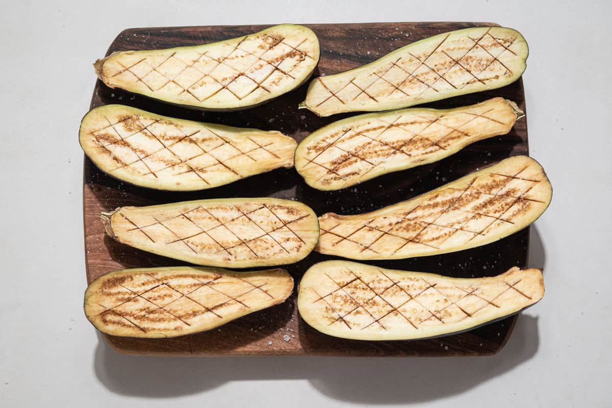 An overhead photo of 8 eggplant halves cut into a diamond cross-hatch pattern on a cutting board.