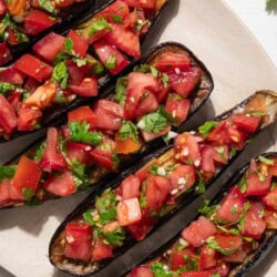 An overhead photo of 5 pieces of eggplant bruschetta on a platter next to a sprig of cilantro.