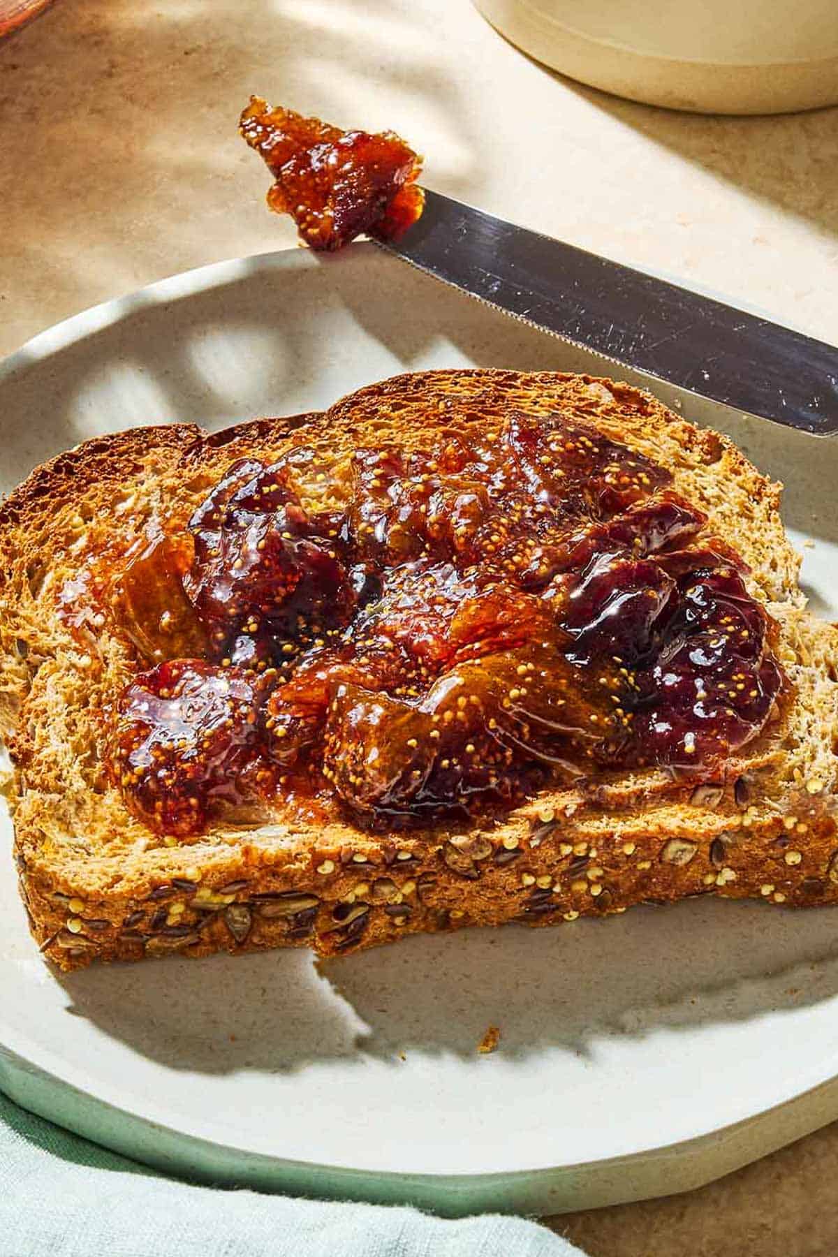 A close up of a piece of toast with fig jam on a plate with a knife.