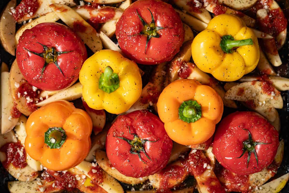 An overhead photo of uncooked gemista greek stuffed vegetables with potato wedges.