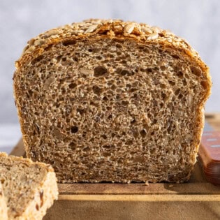 A close up photo of a partially sliced whole wheat bread loaf on a cutting board with a knife.