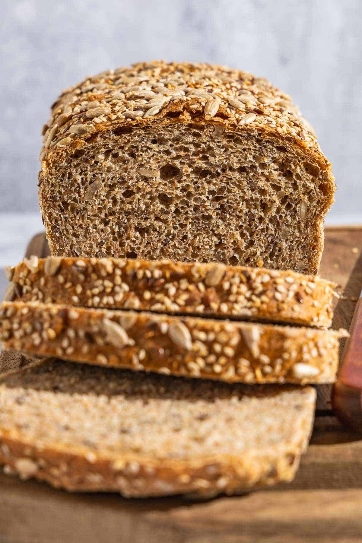 A close up photo of a partially sliced whole wheat bread loaf behind 3 slices of the bread.