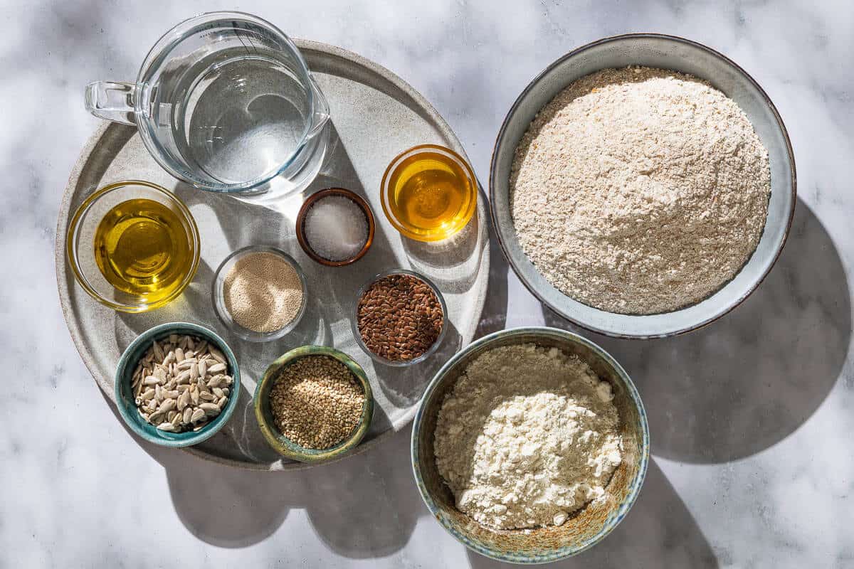 Ingredients for whole wheat bread including flax, sunflower and sesame seeds, whole wheat flour, all purpose flour, salt, instant yeast, water, olive oil and honey.