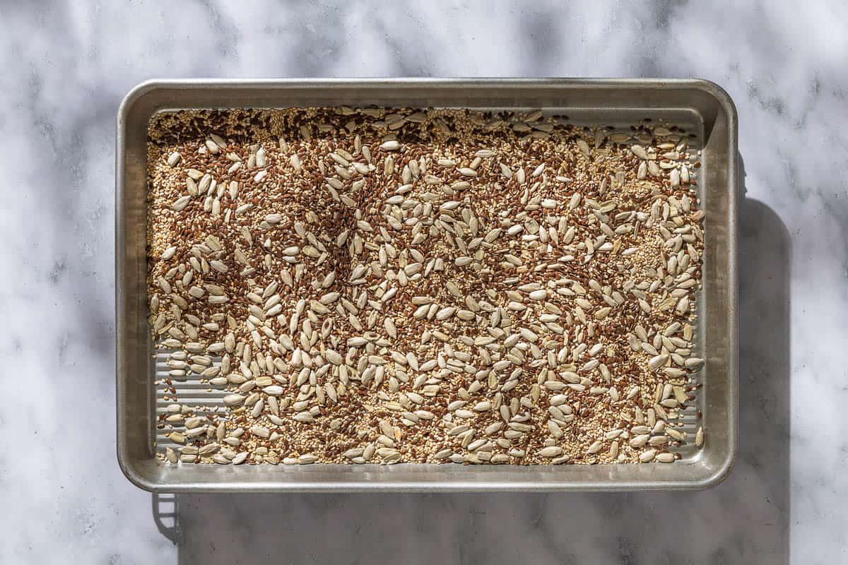 The seeds for the whole wheat bread spread evenly on a baking sheet.