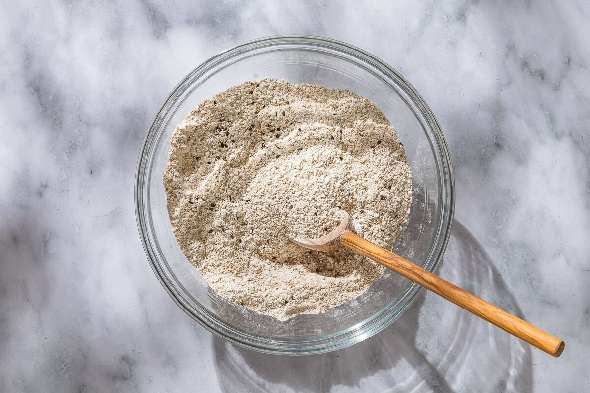 The dry ingredients for the whole wheat bread in a mixing bowl with a wooden spoon.