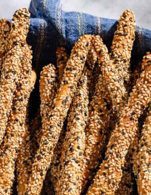 A close up of baked crispy sesame breadsticks in a basket lined with a cloth towel.