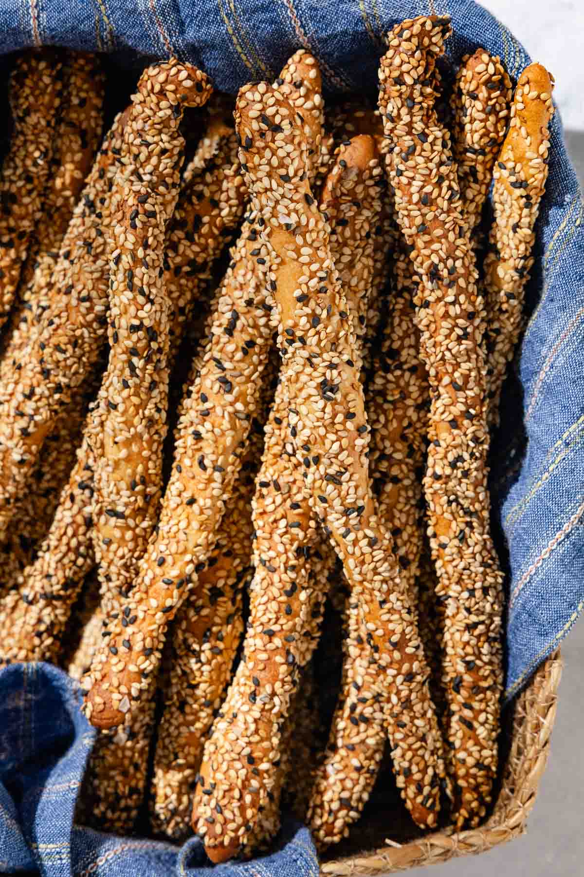 A close up of baked crispy sesame breadsticks in a basket lined with a cloth towel.