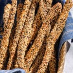 A close up of baked crispy sesame breadsticks in a basket lined with a cloth towel.