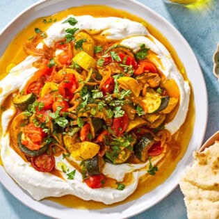 An overhead photo of borani kadoo on a serving plate. Next to this is a plate of pita pieces and a small bowl of chopped herbs.