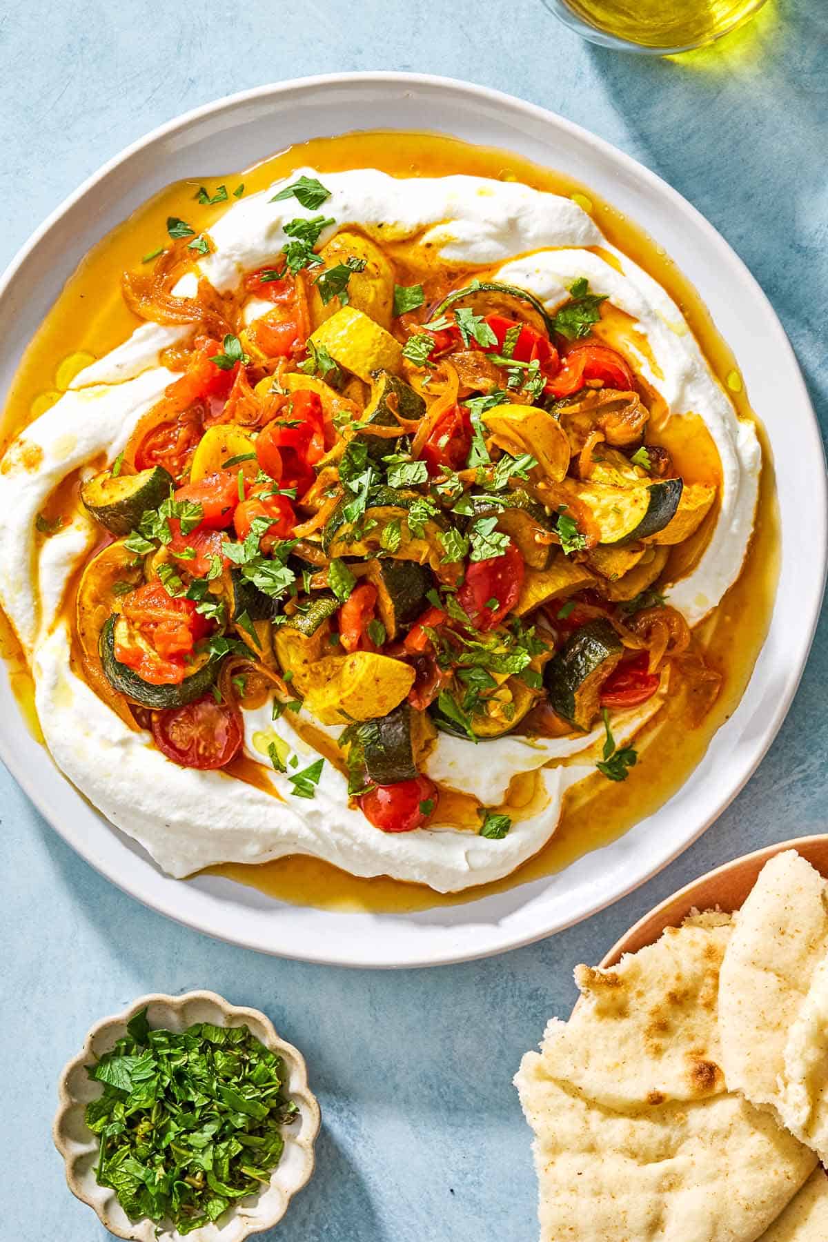 An overhead photo of borani kadoo on a serving plate. Next to this is a plate of pita pieces and a small bowl of chopped herbs.