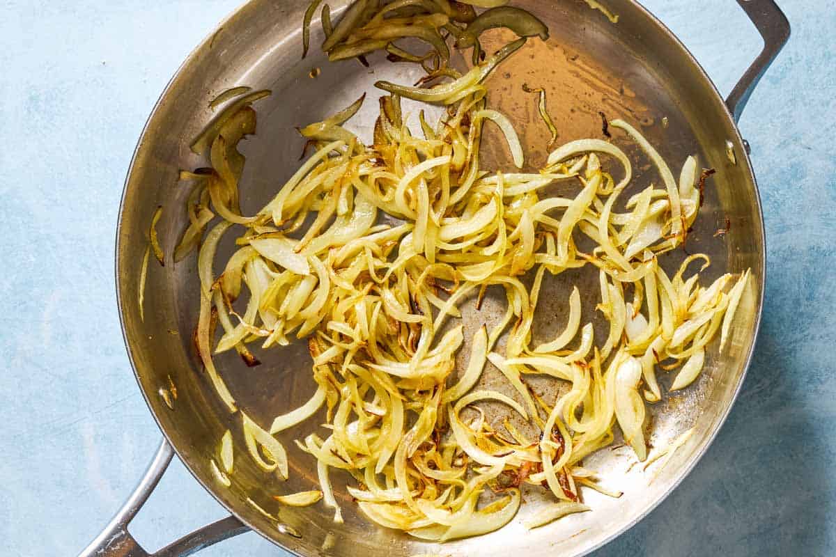 An overhead photo of finely sliced onion being sauteed in a skillet.