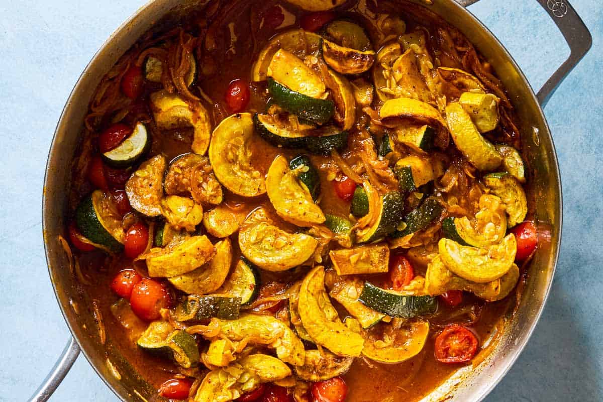 An overhead photo of the tomato sauce and roasted zucchini slices for the borani kadoo simmering together in a skillet.