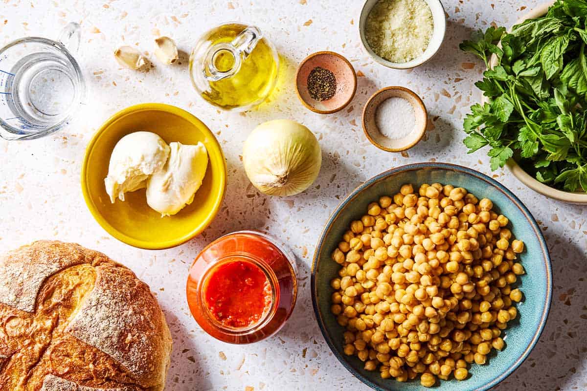 Ingredients for chickpeas in tomato sauce including chickpeas, olive oil, onion, garlic, salt, black pepper, marinara sauce, water, mozzarella, parsley, basil, pecorino romano cheese, and crusty bread.