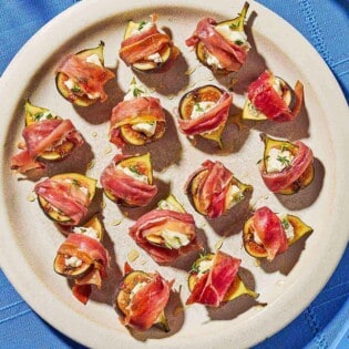 An overhead photo of several prosciutto wrapped figs drizzled with honey on a plate next to a bowl of honey.