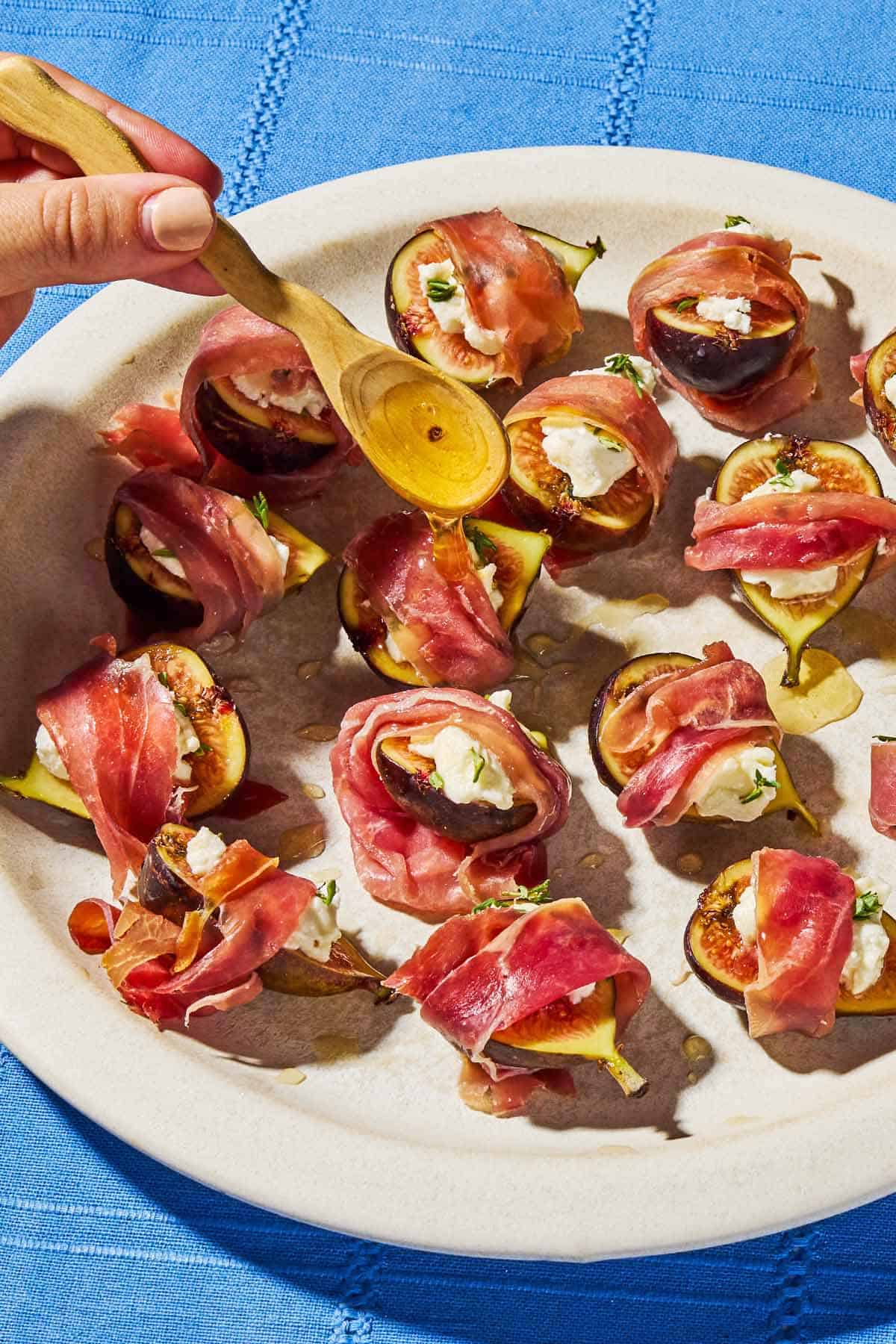 A close up of several prosciutto wrapped figs being drizzled with honey.