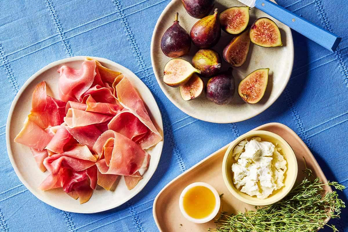 Ingredients for prosciutto wrapped figs including figs, goat cheese, fresh thyme, honey, and prosciutto.