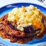 A close up of a serving of Greek Shepherd's Pie on a plate next to a fork.