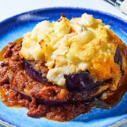 A close up of a serving of Greek Shepherd's Pie on a plate next to a fork.