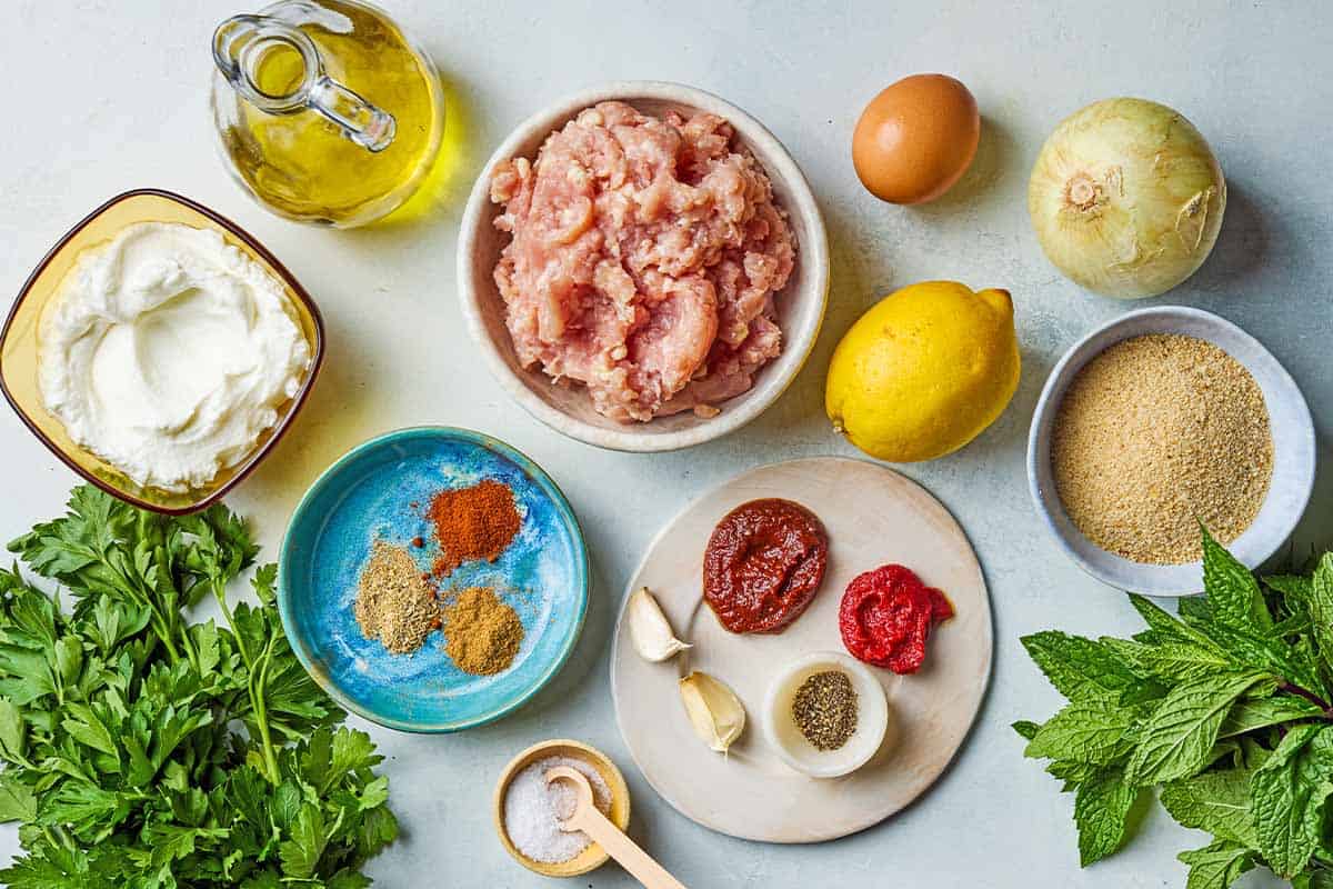 Ingredients for chicken kofta kebabs including ground chicken, breadcrumbs, onion, garlic, parsley, mint, harissa, tomato paste, egg, olive oil, coriander, cumin, sweet paprika, salt, black pepper, greek yogurt, mint, and lemon.