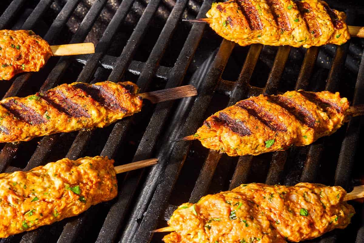 Six grilled chicken kofta kebabs on a grill.