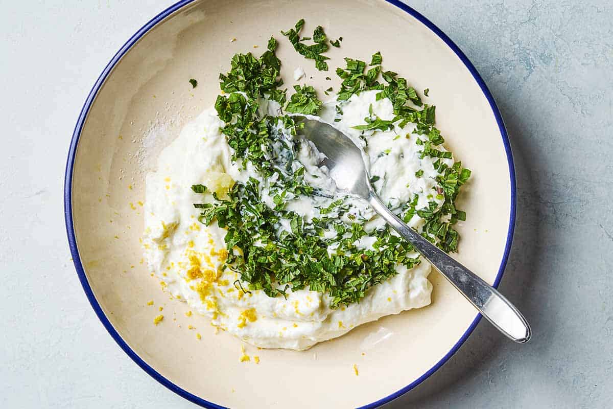 The ingredients for the mint yogurt sauce in a bowl with a spoon, just before being mixed together.