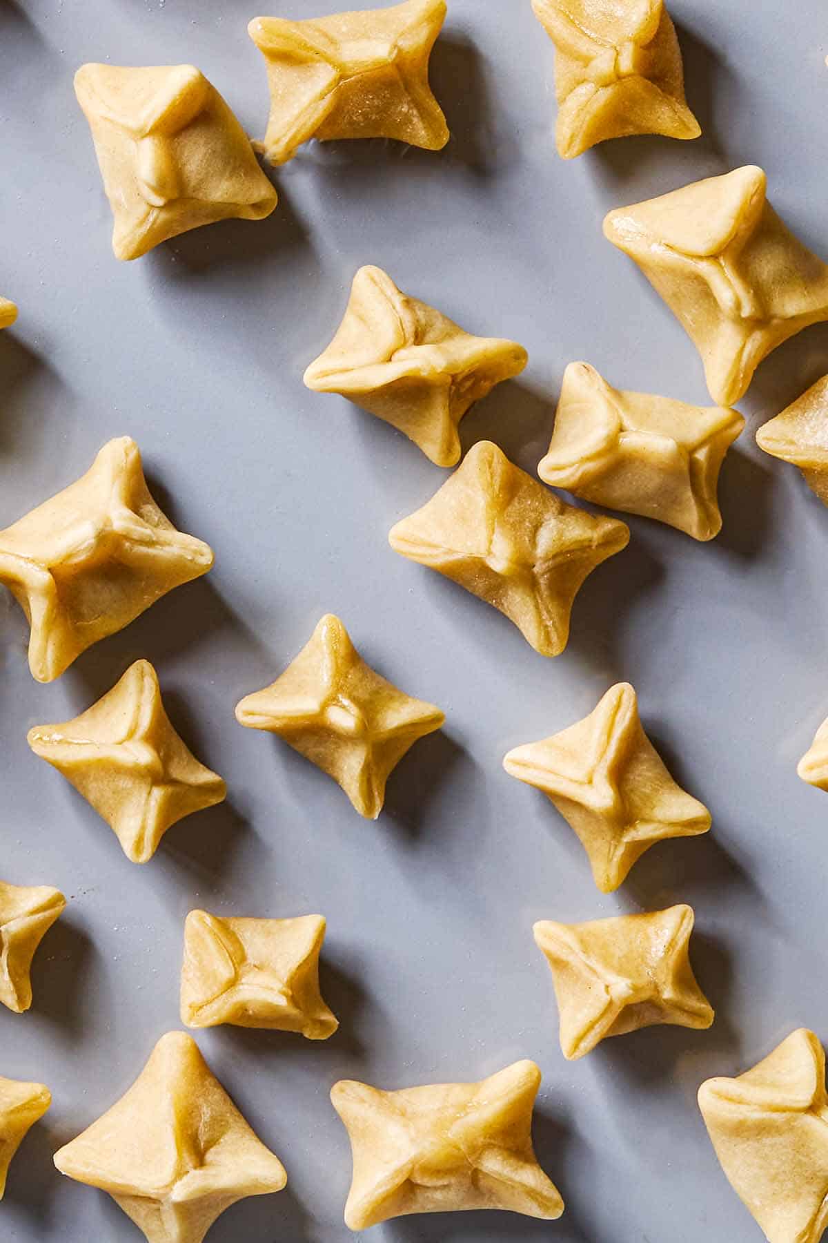 A close up of unboiled sealed manti on a baking sheet.