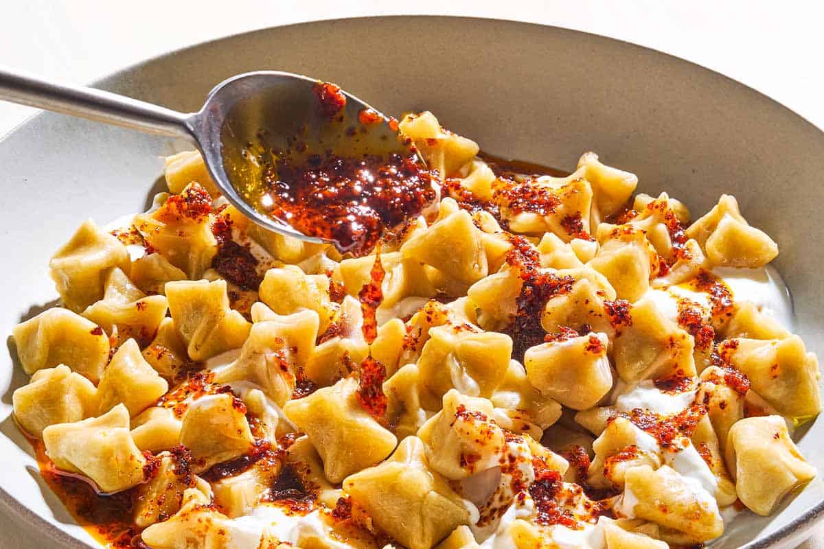 A close up of manti in a bowl being topped with spiced olive oil.