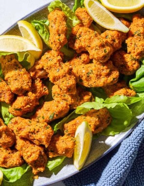 An overhead photo of several turkish lentil patties with lettuce and lemon wedges on a serving platter with a kitchen towel.