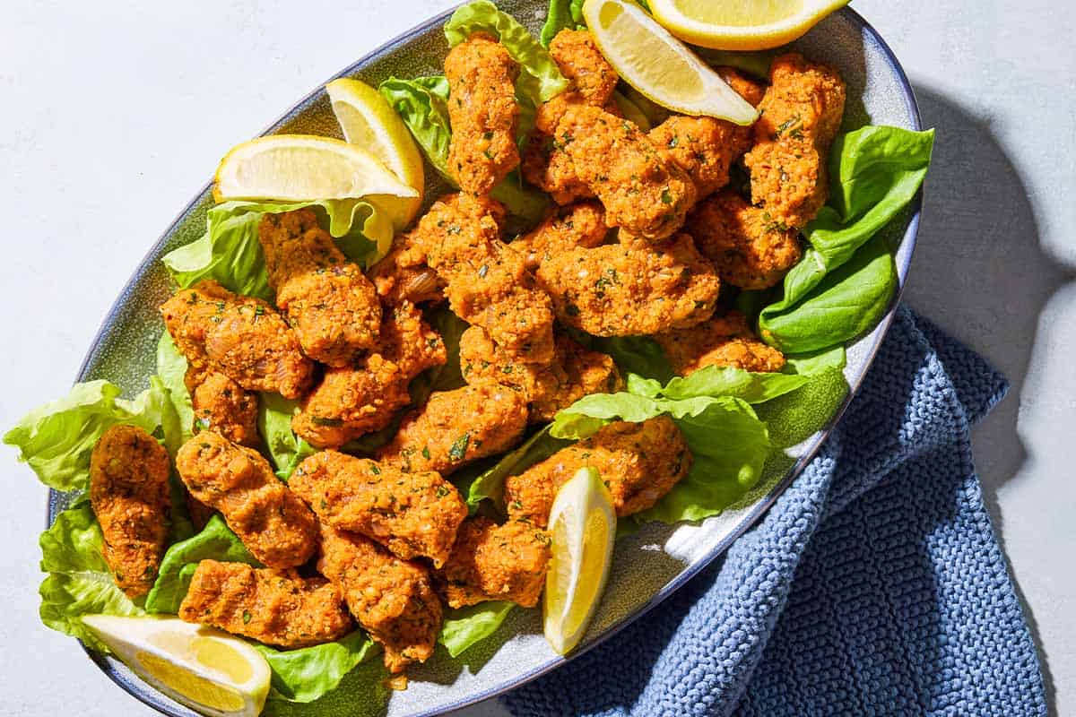 An overhead photo of several turkish lentil patties with lettuce and lemon wedges on a serving platter with a kitchen towel.