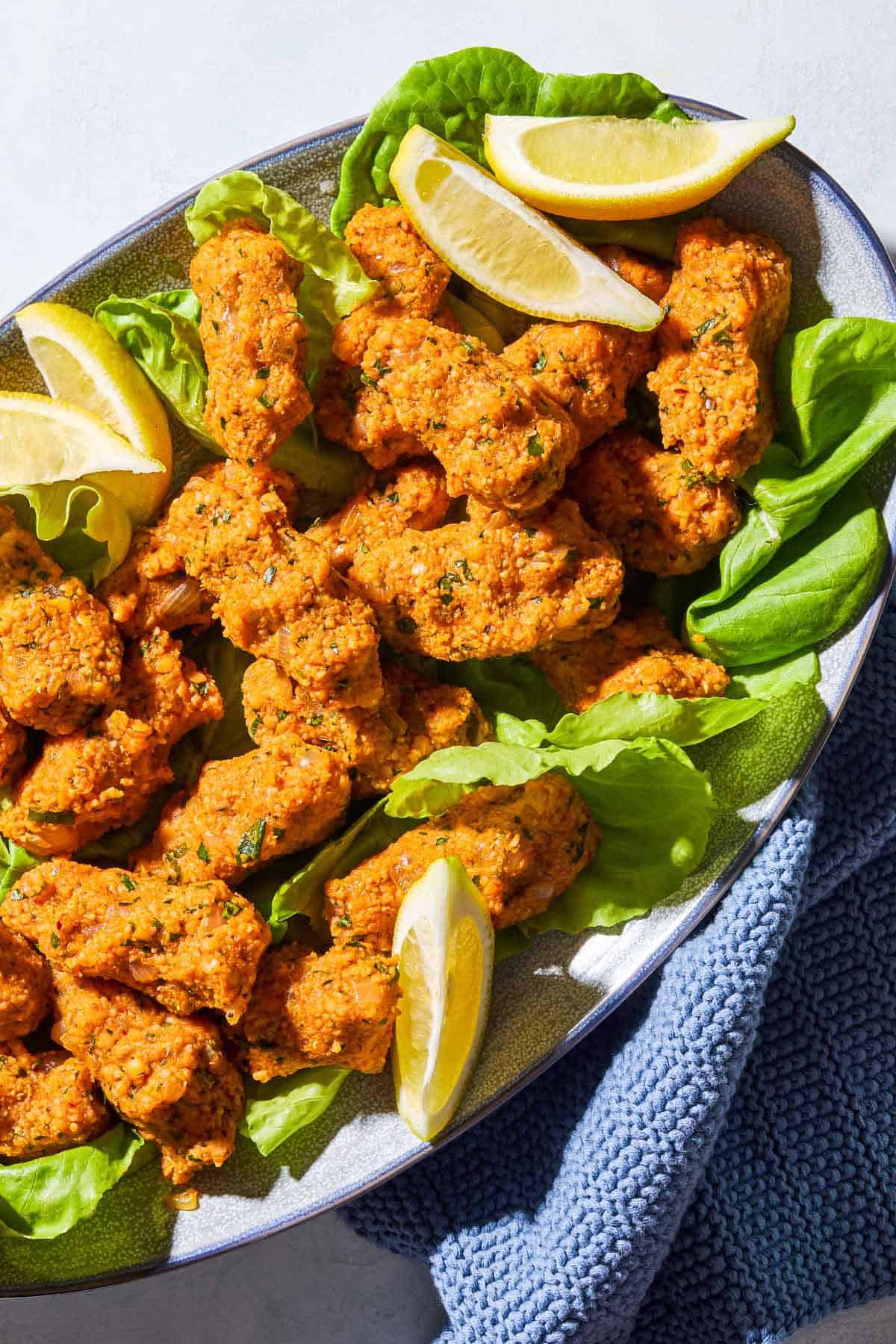 An overhead photo of several turkish lentil meatballs called Mercimek Köftesi with lettuce and lemon wedges on a serving platter next to a kitchen towel.