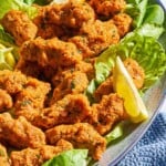 An overhead photo of several turkish lentil patties with lettuce and lemon wedges on a serving platter next to a kitchen towel.