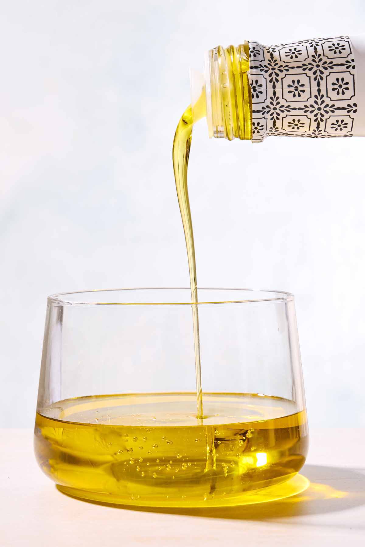 Olive oil being poured from a bottle into a clear bowl.