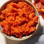 An overhead photo of sun dried tomato pesto in a bowl. Next to this is a cloth napkin, and some cashews and sun dried tomatoes.