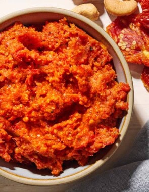 An overhead photo of sun dried tomato pesto in a bowl. Next to this is a cloth napkin, and some cashews and sun dried tomatoes.