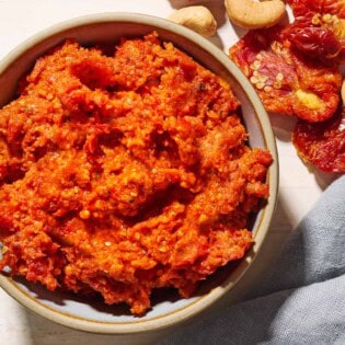 An overhead photo of sun dried tomato pesto in a bowl. Next to this is a cloth napkin, and some cashews and sun dried tomatoes.