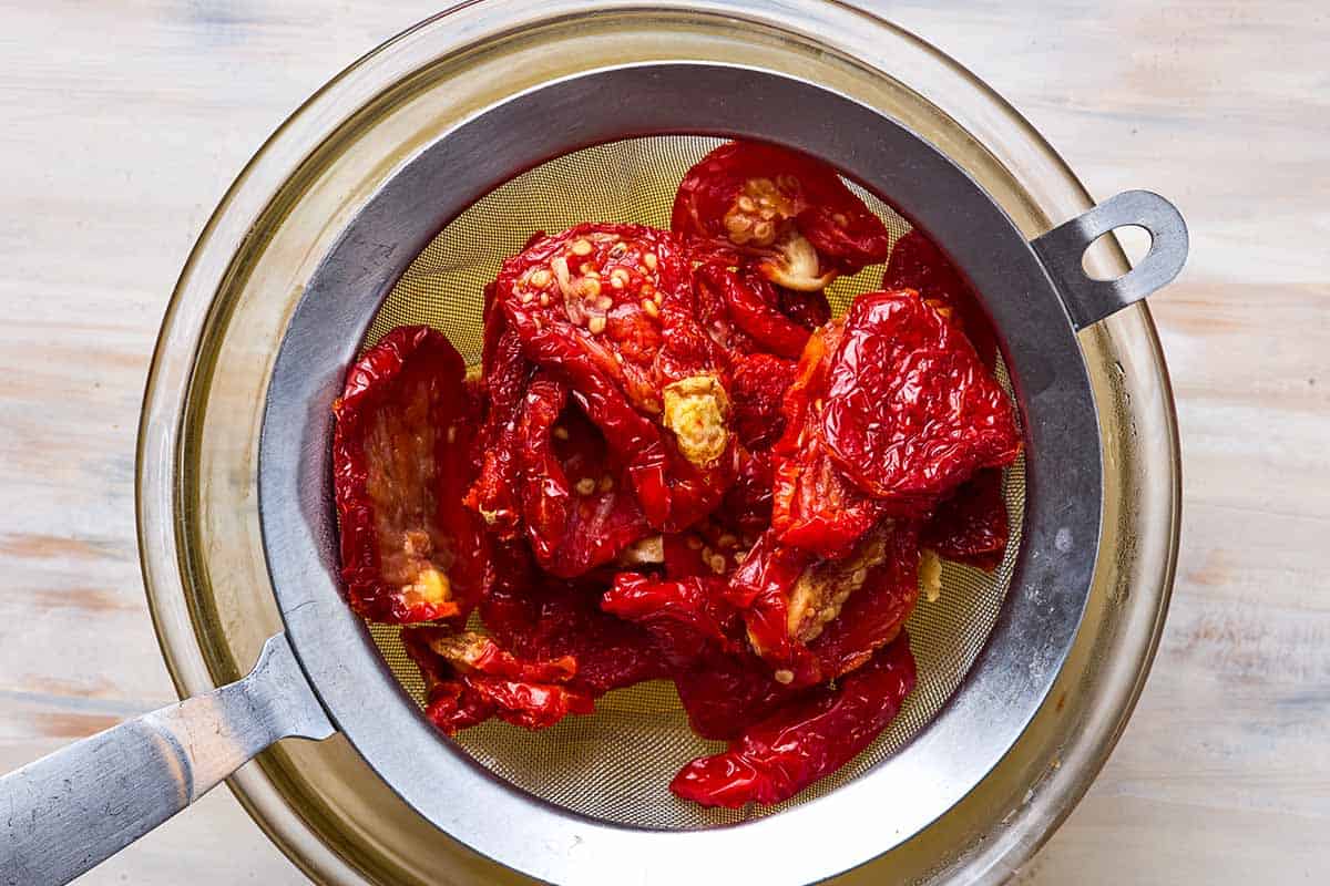 An overhead photo of sun dried tomatoes being drained in a colander sitting over a bowl.