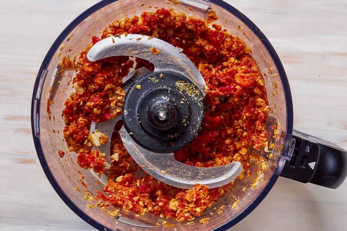 An overhead photo of sun dried tomato pesto in the bowl of a food processor fitted with a blade.