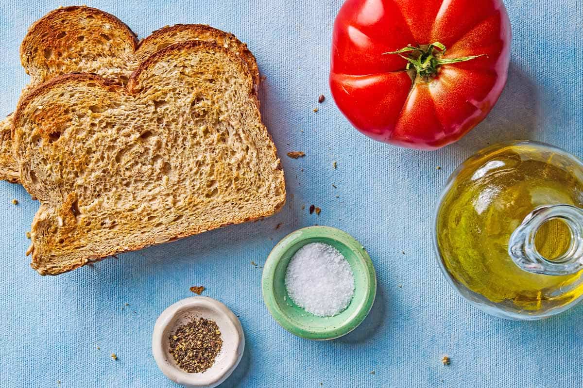 Ingredients for a tomato sandwich including a tomato, 2 slices of toast, olive oil, salt and black pepper.