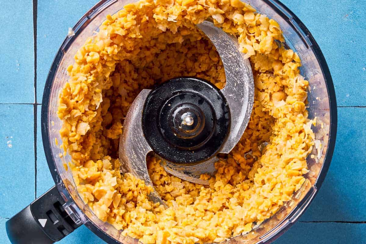 An overhead photo of the the chickpeas and artichokes for the vegetarian crab cakes in the bowl of a food processor fitted with a blade.